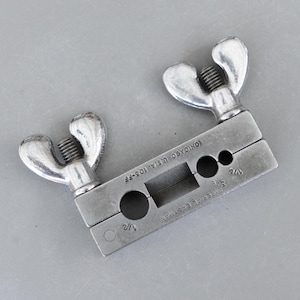 May include: A silver-colored Imperial Eastman flaring tool. The tool has two wing nuts and is marked with "CHICAGO U.S.A. 105-FF". It has openings for 1/2, 3/8, and 1/4 inch tubing. The tool is designed for flaring tubing.