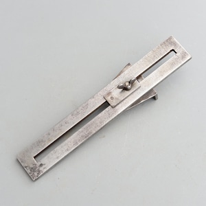 May include: A silver metal tool with a sliding mechanism and a knob for adjusting the width. The tool is used for marking parallel lines.