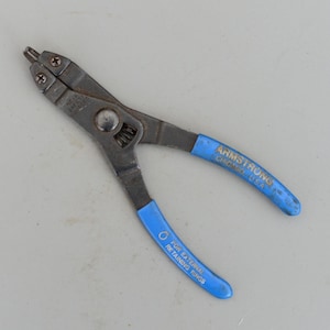 May include: A pair of Armstrong retaining ring pliers with blue handles. The pliers are made of metal and have a spring mechanism. The text "ARMSTRONG CHICAGO U.S.A." is printed on one handle, and "FOR EXTERNAL RETAINING RINGS" is printed on the other.