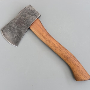 May include: A small hatchet with a weathered steel blade and a curved wooden handle. The blade shows signs of use, and the handle has a natural wood grain finish. The hatchet is designed for chopping and splitting wood.