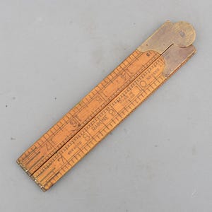 May include: A vintage wooden folding ruler with brass fittings. The ruler is marked with inch measurements and the text "RABONE" and "MADE IN ENGLAND". The ruler is made of boxwood and is approximately 12 inches long when fully extended.