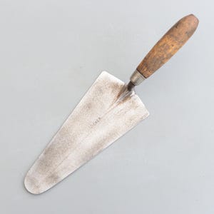 May include: A vintage trowel with a wooden handle and a metal blade. The blade is marked "VICKER".