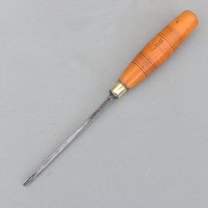 May include: A woodworking tool featuring a wooden handle and a metal blade. The handle is light brown with dark brown rings and the text "L.E.G." The metal blade is silver and narrows to a point.