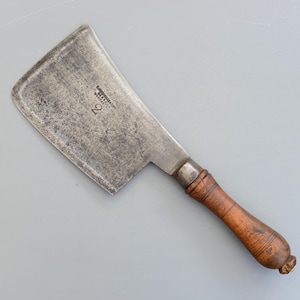May include: A vintage cleaver with a rectangular steel blade and a wooden handle. The blade shows signs of wear and tear, with the number "2" stamped on the surface. The handle is a dark brown colour.