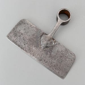 Peut inclure: Un outil métallique rectangulaire vieilli avec une poignée comportant une ouverture circulaire. L'outil a une surface plate en forme de lame et une apparence texturée et vieillie, suggérant qu'il s'agit d'un objet ancien ou vintage. La poignée est fixée à la lame avec un design en forme de cœur.