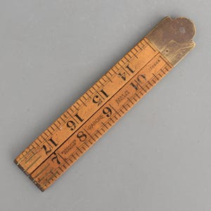 May include: A vintage folding wooden ruler with brass hinges and fittings. The light brown wood features black printed imperial measurement markings and numbers. Text on the ruler includes "Warranted Boxwood", "Rabone", and "Made in England".