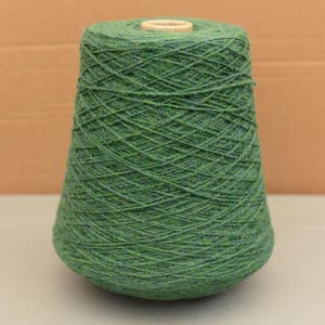 May include: A large cone of green yarn with a wooden core. The yarn is a mix of green shades, creating a textured appearance. The cone shape is ideal for knitting and crochet projects.