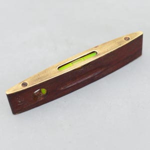 May include: A vintage spirit level with a dark wood body and brass accents. The level features a clear vial with a green bubble, indicating the level of the surface. The tool is designed for measuring horizontal and vertical surfaces.