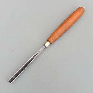 May include: A woodworking chisel with a wooden handle and a metal blade. The handle is a light brown colour, and the blade is silver. The chisel is designed for shaping and carving wood. The chisel is approximately 20 cm long.