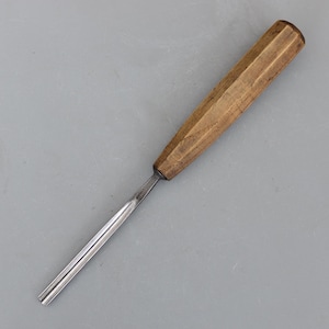May include: A wood carving chisel with a faceted wooden handle and a silver-coloured blade. The chisel is designed for detailed woodworking and carving projects. The handle is a light brown colour.