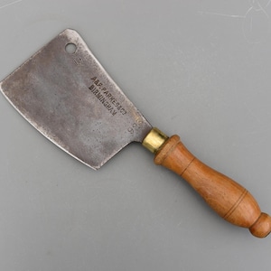 May include: A vintage cleaver with a rectangular steel blade and a wooden handle. The blade has a worn, aged appearance with the text "A.F. PARKES & CO BIRMINGHAM" and the number "36" stamped on it. The handle is attached with a brass ferrule.