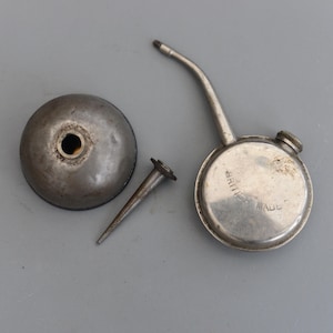 以下が含まれることがあります： 長い注ぎ口と小さなキャップが付いたヴィンテージの銀製のオイル缶。缶には「BRILL」と「MADE」の文字が印刷されています。オイル缶には、小さな銀製のノズルと銀製のキャップが付いています。