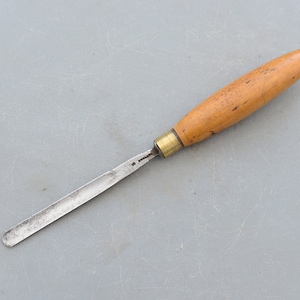 Op de afbeelding: Een houtsnijgereedschap met een houten handvat en een metalen mes. Het gereedschap is ongeveer 30 cm lang.