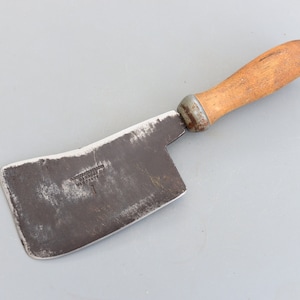 Puede incluir: Un cuchillo de carnicero vintage de metal oxidado con mango de madera. La hoja es curva y tiene un pequeño agujero rectangular cerca del mango. El mango es marrón y tiene una ligera curva.