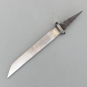May include: A vintage, small, metal knife with a long, silver blade and a dark, pointed tip. The knife has a rectangular bolster and a slightly worn appearance, suggesting age and use. The blade is approximately 6 inches long.