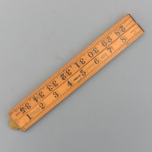 May include: A vintage wooden folding ruler, measuring up to 36 inches. The ruler is light brown with black markings and the text "RABONE" and "MADE IN ENGLAND". The ruler is folded and has a brass hinge.