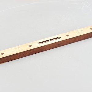 May include: A vintage wooden level with brass end caps and insets. The level has two bubble vials and is marked with text. The wood is a rich brown colour, and the brass has a golden hue. A classic tool.