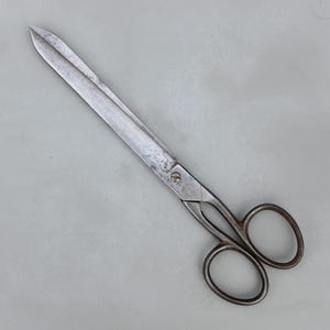Puede incluir: Tijeras de metal vintage con una hoja larga y puntiaguda y dos bucles para los dedos. Las tijeras tienen un aspecto desgastado y envejecido. Las hojas miden aproximadamente 25 cm de largo.