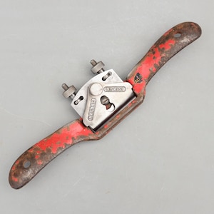 May include: A vintage hand scraper tool with a red painted handle and a silver blade holder. The handle shows signs of wear and rust. The blade holder is marked "RECORD" and "NRA 51".