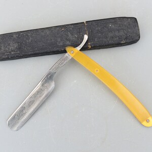 Può includere: Un rasoio a mano libera vintage con manico in plastica gialla e lama in argento. Il rasoio è in un astuccio in pelle nera.