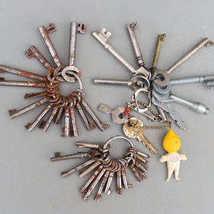 Puede incluir: Una gran colección de llaves vintage en dos llaveros. Las llaves son de metal y tienen una variedad de formas y tamaños. Algunas de las llaves están oxidadas y tienen un acabado de pátina. Los llaveros están unidos a una pequeña figurita de plástico amarilla.