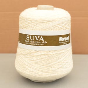 Könnte beinhalten: Eine große Spule cremefarbener Wolle. Das Etikett lautet "SUVA Wool with cotton slub KNITS AS FINE FOUR PLY". Die Spule enthält ca. 2230 Meter Garn, geeignet für Strickprojekte.