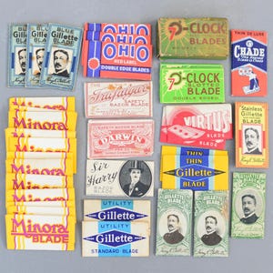 Puede incluir: Una colección de envases de cuchillas de afeitar vintage en varios colores. Las marcas incluyen Gillette, Minora, Ohio, y otras. El embalaje presenta ilustraciones, texto y retratos, mostrando el diseño histórico de los productos de afeitado.