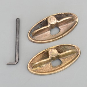 Puede incluir: Dos pomos de puerta ovalados de latón con un pequeño agujero en el centro y una forma de cruz en relieve en la parte superior. También se incluye una pequeña varilla de metal.