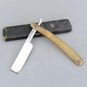 以下が含まれることがあります： 骨製のハンドルと黒い革製のケースが付いたヴィンテージのストレートシェービングナイフ。ナイフは銀の刃で、「Made in Sheffield, England」という文字が刻まれています。