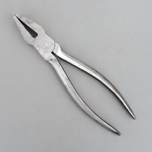 Peut inclure: Une pince argentée avec un tranchant noir. L'outil a une poignée incurvée et un point de pivot central. Ces pinces sont conçues pour saisir et couper des matériaux, couramment utilisées.