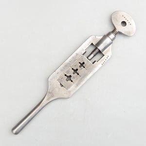 May include: A vintage metal pipe threading tool with a key handle and a numbered scale. The tool has four different sized dies for threading pipes.