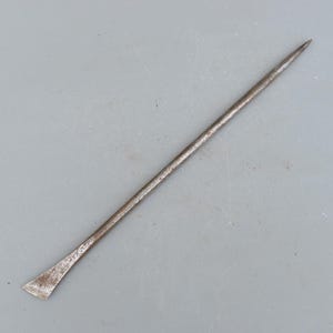 Könnte beinhalten: Ein langes, dünnes Werkzeug aus Metall mit einem spitzen Ende und einer flachen, leicht gebogenen Klinge. Das Werkzeug ist aus stumpfem, grauem Metall und weist eine leicht rostige Optik auf.