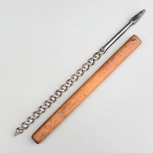 Może przedstawiać: Długi, srebrny wiertło z drewnianym uchwytem. Wiertło jest skręcone i ma ostry czubek. Uchwyt jest brązowy i ma gładką powierzchnię.