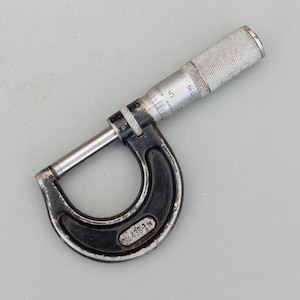 May include: A vintage black and silver micrometer, a precision measuring tool. The micrometer has a U-shaped frame, a rotating thimble, and a spindle for accurate measurements. The tool has the text "No. 436-1 in" on the frame.
