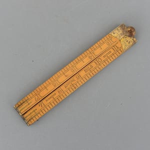 May include: A vintage wooden folding ruler, featuring inch markings from 7 to 18. The ruler is made of boxwood and has the text "RABONE 9" and "MADE IN ENGLAND" printed on it. The ruler is approximately 18 inches long when fully extended.