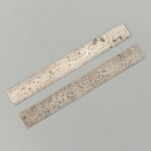 Peut inclure: Deux règles métalliques vintage avec des marquages de mesure. Les règles sont marquées de chiffres et de lignes pour des mesures précises. Les règles sont en métal de couleur argentée et présentent des signes d'usure et de vieillissement.