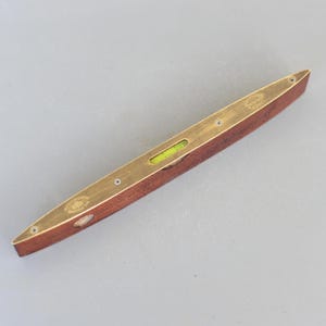 Pode incluir: Um nível de latão com base de madeira e um nível de bolha verde. O nível mede aproximadamente 30 cm de comprimento.