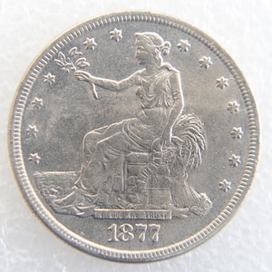 Puede incluir: Una moneda de plata con una figura femenina sentada sosteniendo una rama, con la palabra "LIBERTY" visible. La moneda está fechada en 1877 e incluye la inscripción "IN GOD WE TRUST". La moneda tiene un diseño detallado y forma circular.