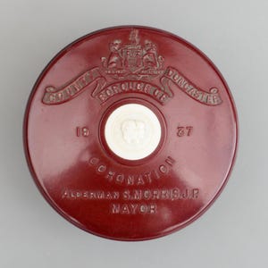 Puede incluir: Un objeto conmemorativo redondo de color granate con texto en relieve y un medallón blanco central. El texto dice "COUNTY BOROUGH OF DONCASTER", "CORONATION" y "ALDERMAN S. MORRIS J.P. MAYOR", con los años "19" y "37".