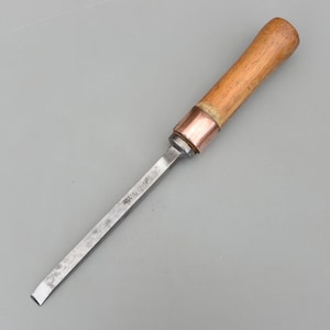 Könnte beinhalten: Ein Holzbeitel mit Holzgriff und Metallklinge. Der Griff ist hellbraun und die Klinge silbern. Eine kupferfarbene Zwinge verbindet Griff und Klinge.