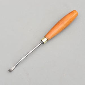 Può includere: Una sgorbia per intaglio del legno con una lama curva. L'utensile ha un manico in legno lucido e una lama in metallo. Il manico è di colore marrone chiaro e la lama è argentata. La sgorbia è progettata per lavori di falegnameria dettagliati.