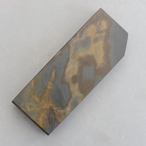 May include: A rectangular sharpening stone with a dark grey, blue, and brown marbled pattern. The stone has a slightly rounded edge on one side.