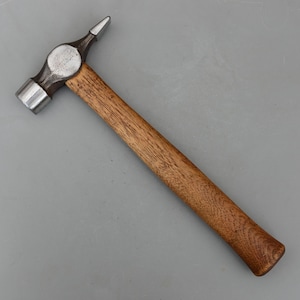 May include: A metal hammer with a wooden handle. The hammer head has a flat striking surface on one side and a pointed tip on the other. The handle is made of light brown wood.