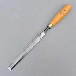 May include: A Marples wood chisel with a long, rectangular steel blade showing signs of wear and a light-colored wooden handle. The handle features a brass ferrule and the brand name Marples printed in a black rectangular border on the wood.