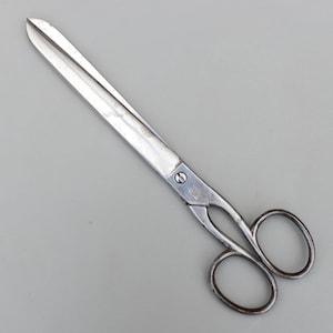 Pode incluir: Um par de tesouras grandes, prateadas, com orifícios redondos para os dedos. As lâminas são longas e retas, com uma ponta. As tesouras são feitas de metal e são projetadas para cortar. Medem cerca de 25 cm de comprimento.