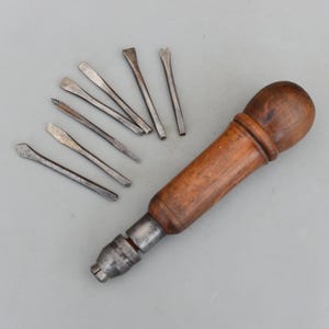 May include: A collection of antique tools, including a wooden-handled screwdriver and several small metal pry bars. The screwdriver has a dark wooden handle and a metal tip. The pry bars are various shapes and sizes.