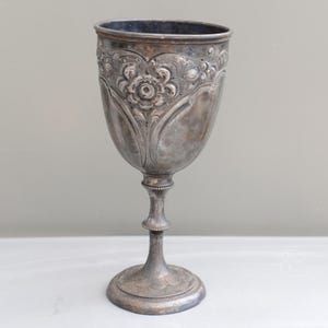 以下が含まれることがあります： 装飾的な花のディテールが施された、ヴィンテージの銀のゴブレット。ゴブレットは、広いボウル、ビーズのアクセントが付いた細いステム、円形のベースが特徴です。銀は変色した外観で、そのアンティークな魅力を高めています。