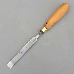 Könnte beinhalten: Ein Stecheisen mit einem hellbraunen Holzgriff und einer Metallklinge. Die rechteckige Klinge hat eine silberne Oberfläche. Der Griff ist mit einer Messingzwinge an der Klinge befestigt. Das Stecheisen ist für die Holzbearbeitung.