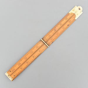 以下が含まれることがあります： ヴィンテージの木製折りたたみ定規。センチメートル単位の刻印と真鍮製のヒンジが特徴です。定規は薄茶色で、両端は白。最大61cmまで測定できます。木工や工芸に適した、クラシックで機能的なデザインです。