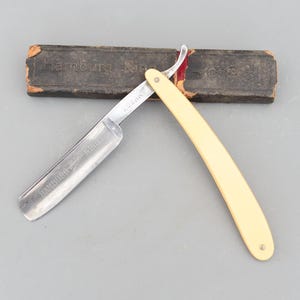 以下が含まれることがあります： 白いプラスチック製のハンドルと銀色の刃を持つヴィンテージのストレートシェーバー。刃には「HAMBURGER - FAKU」と「ROBER.」が刻印されています。シェーバーは、「Hamburg - R.」という刻印のある黒い革ケースに入っています。